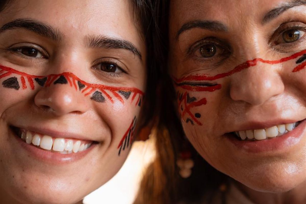 Duas visitantes sorrindo com pintura facial indígena durante a visita à aldeia