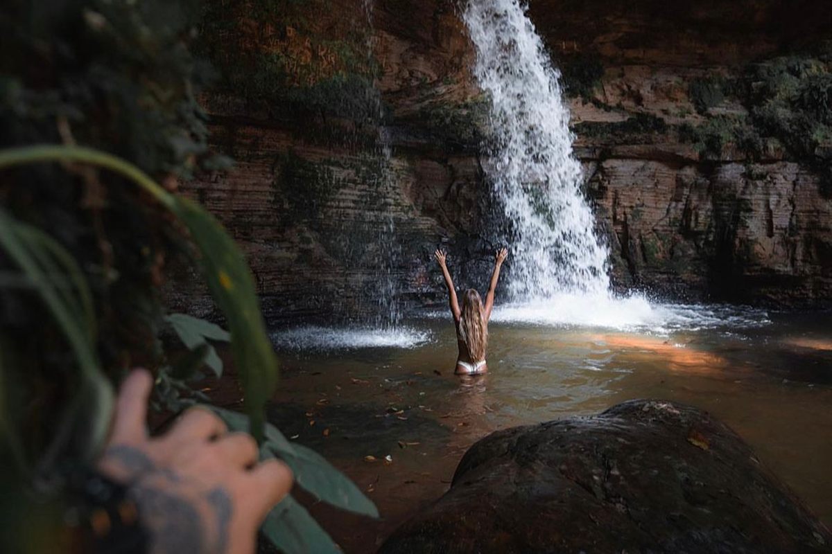 Visitante de braços erguidos diante de uma cachoeira em um poço na mata de Presidente Figueiredo